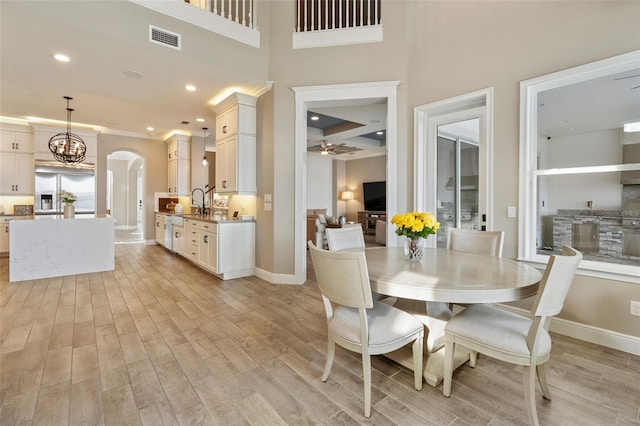 dining area with crown molding, sink, ceiling fan with notable chandelier, and light hardwood / wood-style flooring