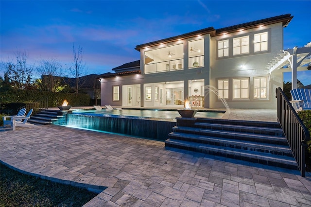 back house at dusk featuring a fenced in pool, a patio area, a balcony, and ceiling fan