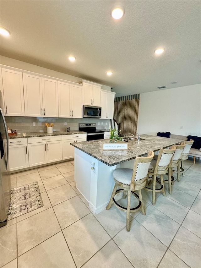 kitchen featuring a breakfast bar, a center island with sink, dark stone countertops, appliances with stainless steel finishes, and white cabinets