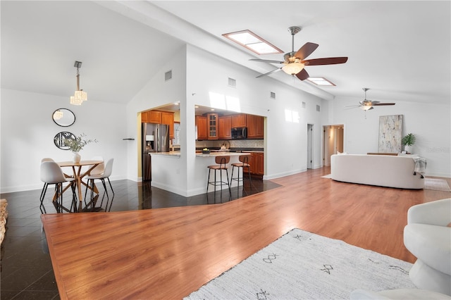 living room with dark wood-type flooring, ceiling fan, a skylight, and high vaulted ceiling