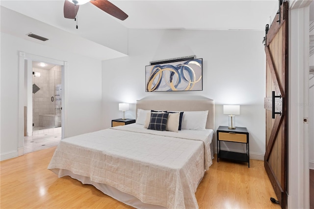 bedroom with vaulted ceiling, a barn door, ensuite bathroom, and light hardwood / wood-style flooring