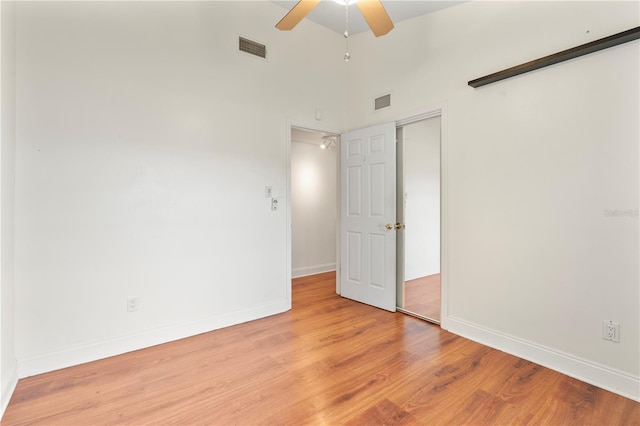 unfurnished bedroom with a high ceiling, ceiling fan, light wood-type flooring, and a closet