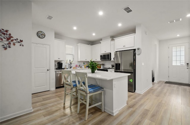 kitchen with a kitchen bar, a center island, light hardwood / wood-style flooring, appliances with stainless steel finishes, and white cabinets