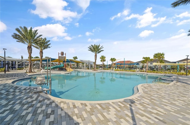 view of swimming pool with a water slide, a patio area, and a hot tub