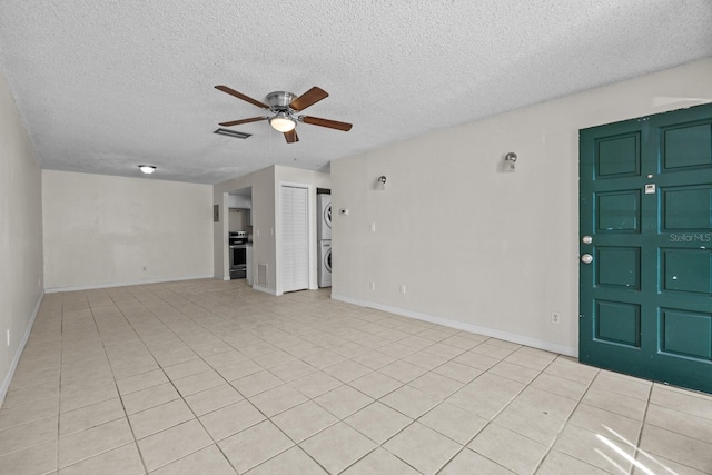 interior space with ceiling fan, stacked washing maching and dryer, a textured ceiling, and light tile patterned floors