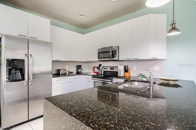 kitchen with pendant lighting, sink, appliances with stainless steel finishes, white cabinetry, and dark stone countertops