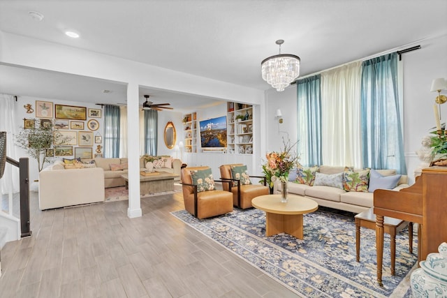 living room with ceiling fan with notable chandelier, built in features, and light hardwood / wood-style flooring