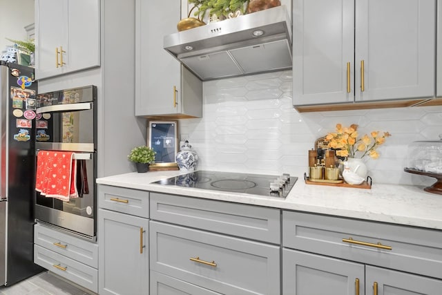 kitchen with gray cabinetry, black electric stovetop, light stone counters, and decorative backsplash