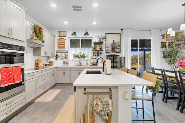 kitchen featuring sink, a breakfast bar area, hanging light fixtures, a center island with sink, and stainless steel double oven