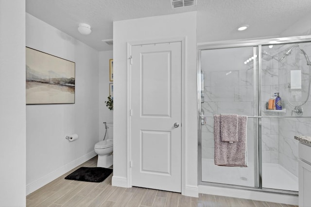 bathroom featuring toilet, a shower with shower door, and a textured ceiling