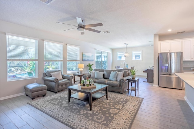 living room featuring a textured ceiling, light wood-style floors, visible vents, and ceiling fan