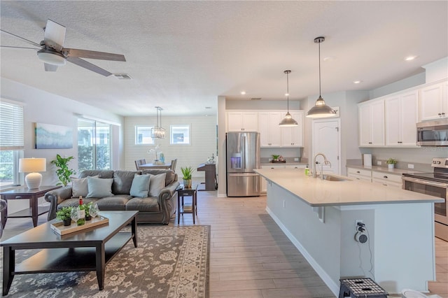 kitchen featuring an island with sink, light countertops, appliances with stainless steel finishes, white cabinets, and a sink