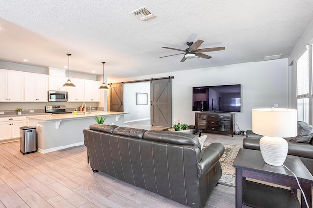 living room featuring visible vents, a ceiling fan, light wood-type flooring, and a barn door