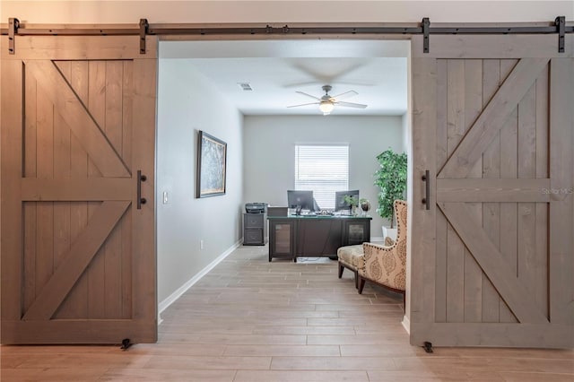 home office with a barn door, light wood-style floors, and a ceiling fan