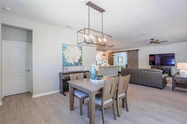 dining room featuring visible vents, baseboards, light wood-type flooring, a barn door, and ceiling fan with notable chandelier