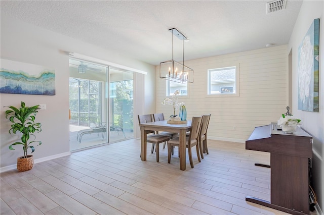 dining room with visible vents, a notable chandelier, a textured ceiling, light wood finished floors, and baseboards