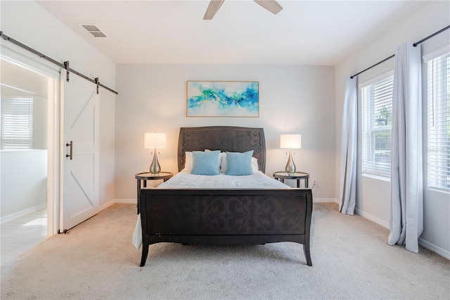 bedroom with visible vents, light carpet, a barn door, baseboards, and ceiling fan