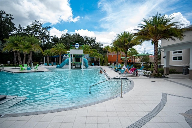 view of swimming pool with a water slide, a playground, and a patio