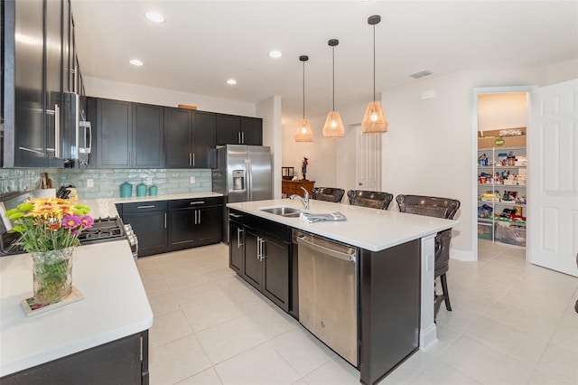 kitchen featuring pendant lighting, a breakfast bar, appliances with stainless steel finishes, a kitchen island with sink, and decorative backsplash