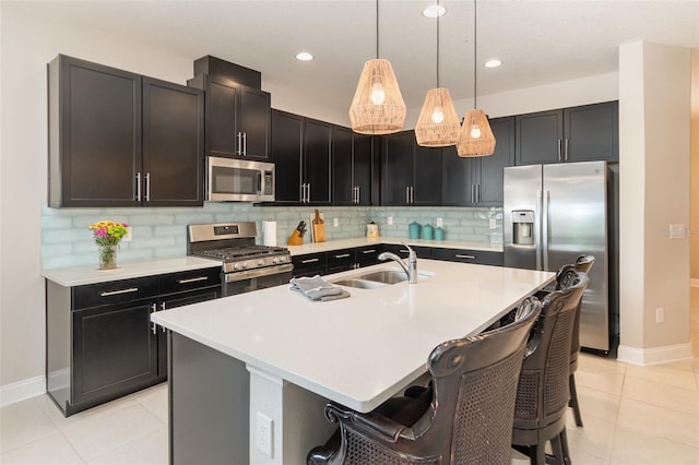 kitchen featuring a breakfast bar, an island with sink, sink, hanging light fixtures, and stainless steel appliances