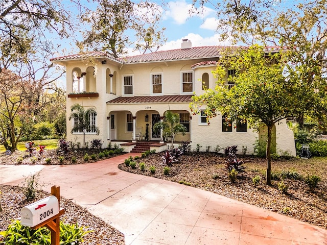 mediterranean / spanish-style house featuring a tile roof, a chimney, a porch, and stucco siding