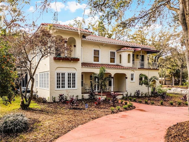 mediterranean / spanish house with a balcony, stucco siding, a porch, and a tiled roof