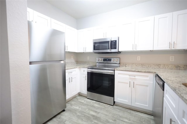 kitchen with stainless steel appliances, white cabinetry, light stone countertops, and light hardwood / wood-style floors