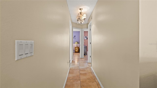 corridor featuring light tile patterned floors, a textured ceiling, and a chandelier