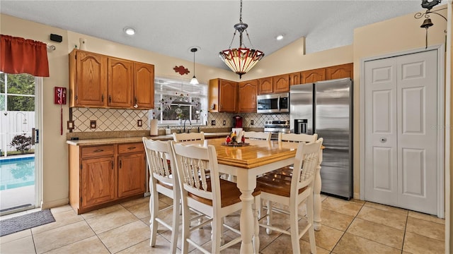 kitchen with vaulted ceiling, pendant lighting, backsplash, light tile patterned floors, and stainless steel appliances