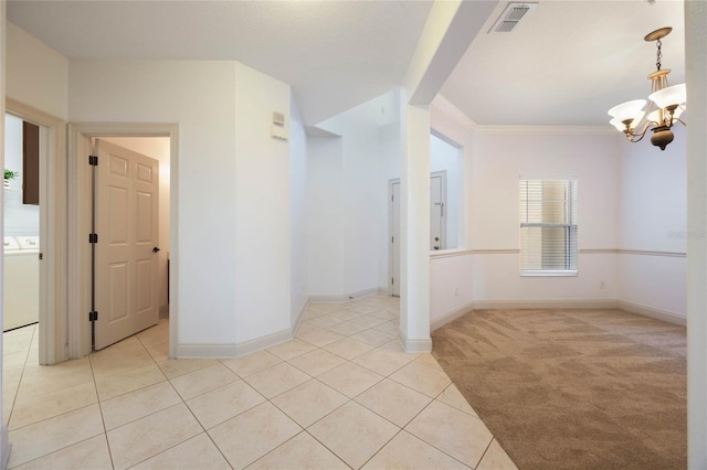 empty room featuring a notable chandelier, washer / dryer, ornamental molding, and light colored carpet