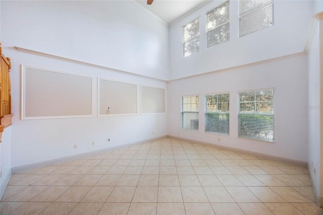 empty room with crown molding, light tile patterned floors, a high ceiling, and a wealth of natural light