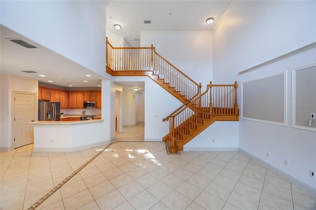 kitchen featuring light tile patterned floors, ornamental molding, appliances with stainless steel finishes, kitchen peninsula, and a high ceiling