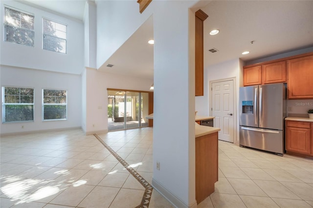 kitchen featuring stainless steel refrigerator with ice dispenser, a towering ceiling, dishwasher, and light tile patterned floors