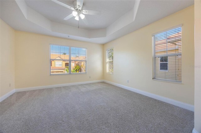 carpeted spare room with a raised ceiling and ceiling fan