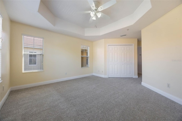 unfurnished bedroom with a tray ceiling, carpet floors, a closet, and ceiling fan