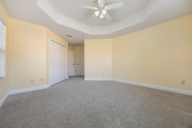 spare room featuring a raised ceiling, ceiling fan, and carpet flooring