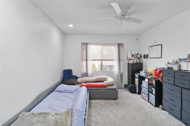 bedroom with ceiling fan, light colored carpet, and a textured ceiling