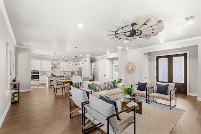 living room with an inviting chandelier, light hardwood / wood-style flooring, ornamental molding, and french doors