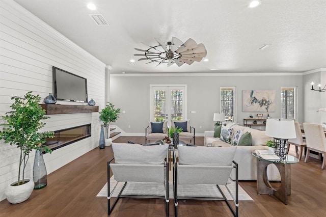 living room featuring french doors, dark wood-type flooring, a chandelier, a textured ceiling, and ornamental molding