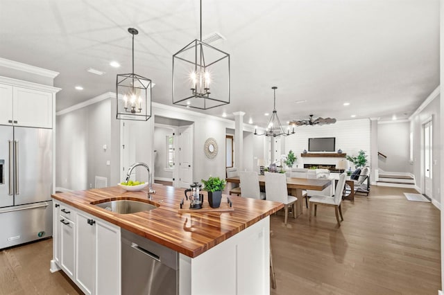 kitchen with sink, butcher block countertops, decorative light fixtures, appliances with stainless steel finishes, and a kitchen island with sink