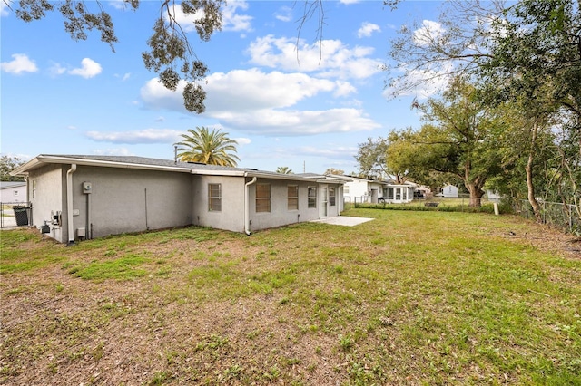 back of property with stucco siding, a lawn, and fence