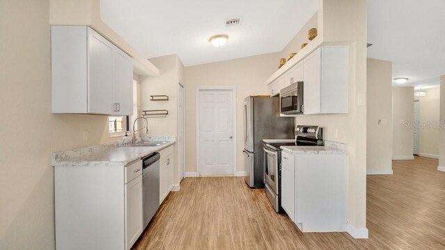 kitchen with appliances with stainless steel finishes, white cabinetry, light hardwood / wood-style flooring, and sink