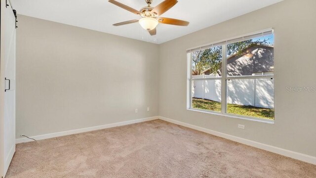 unfurnished room with light carpet, ceiling fan, and a barn door