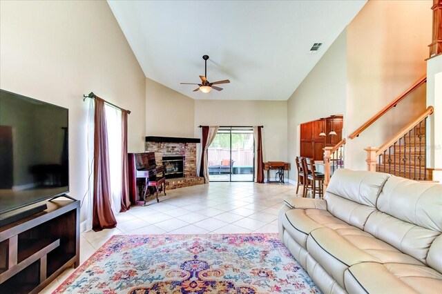 living area with a ceiling fan, a glass covered fireplace, high vaulted ceiling, and light tile patterned floors