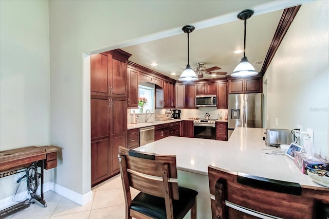 kitchen with decorative light fixtures, light countertops, appliances with stainless steel finishes, a peninsula, and a kitchen breakfast bar