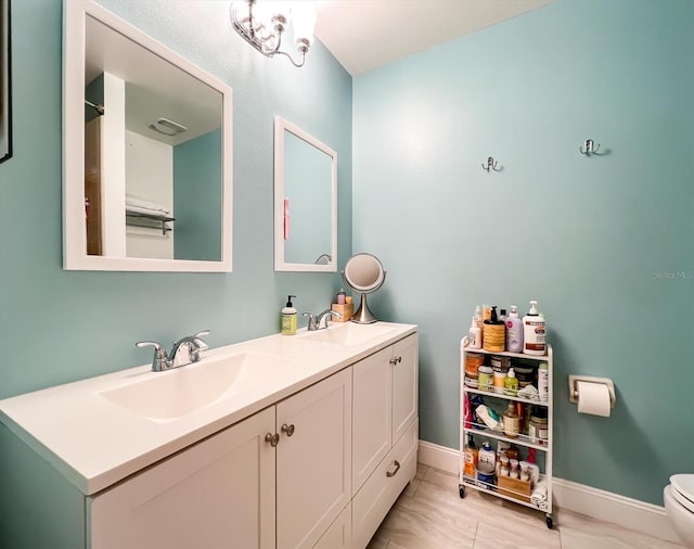 full bath with toilet, double vanity, baseboards, and a sink