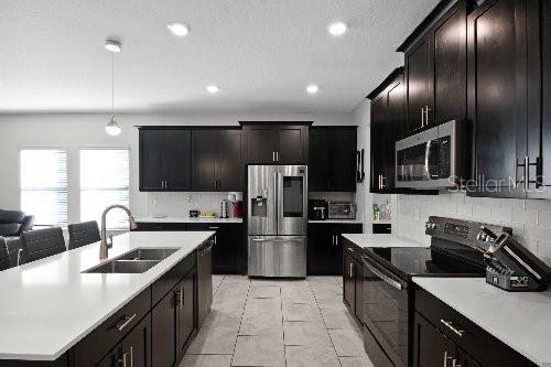 kitchen with appliances with stainless steel finishes, pendant lighting, tasteful backsplash, sink, and a center island with sink