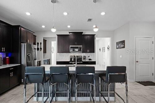 kitchen featuring sink, a center island with sink, appliances with stainless steel finishes, pendant lighting, and backsplash