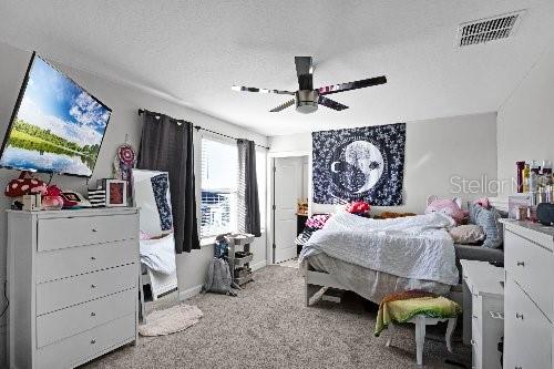 carpeted bedroom with ceiling fan and a textured ceiling