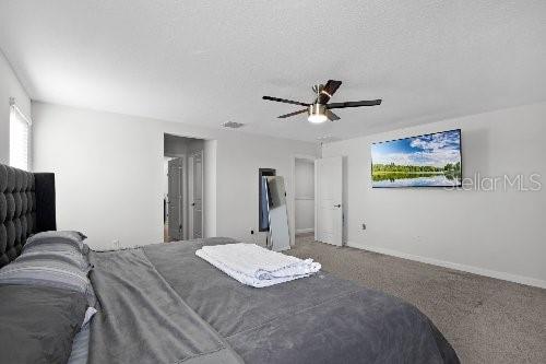 carpeted bedroom featuring ceiling fan and a textured ceiling